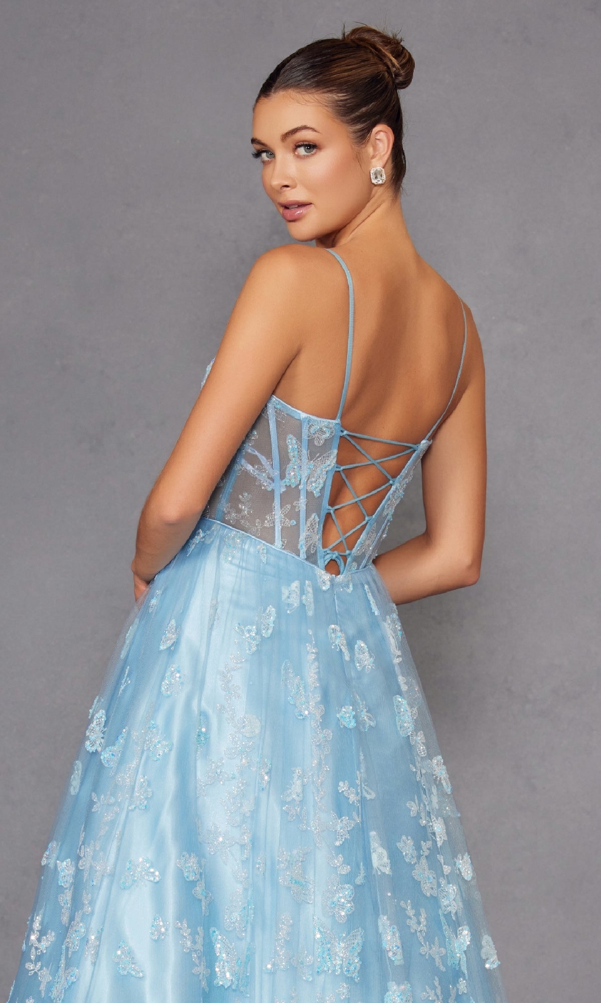 Woman wearing the Sheer-Corset Glitter-Print Long Prom Dress 2413, featuring light blue lace details, thin straps, and a lace-up back, posing against a plain gray background.